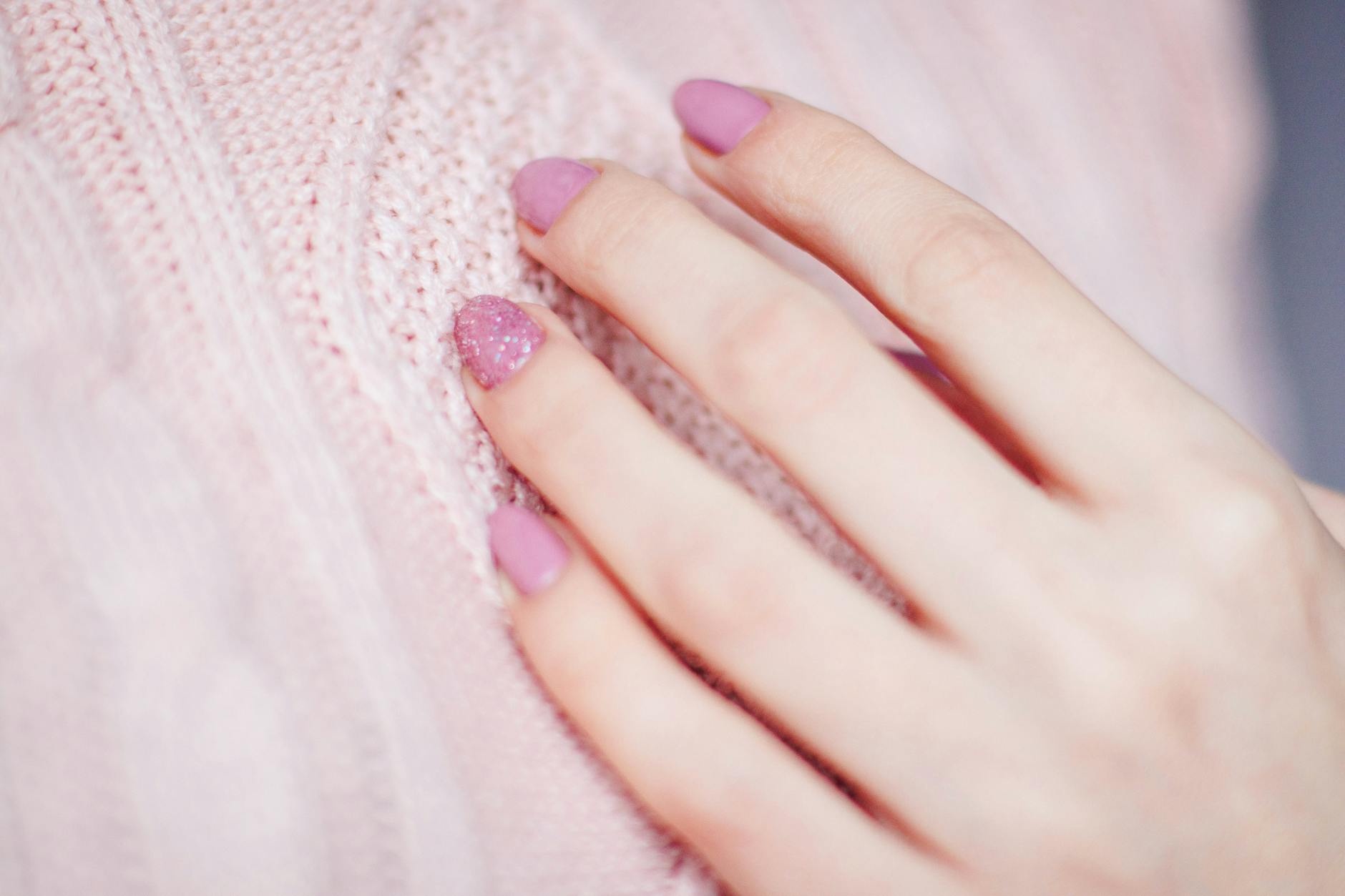 Pomysły na subtelne zdobienia paznokci na ważne spotkania i rozmowy o pracę Dłoń kobiety z subtelnym różowym manicure oparta na miękkim swetrze